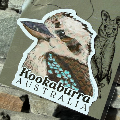 A die-cut sticker featuring a detailed illustration of a kookaburra with the text 'Kookaburra AUSTRALIA' printed below it, attached to a backing card. The backing card also shows a line drawing of a wallaroo and the partial text 'Aussie Mag'.