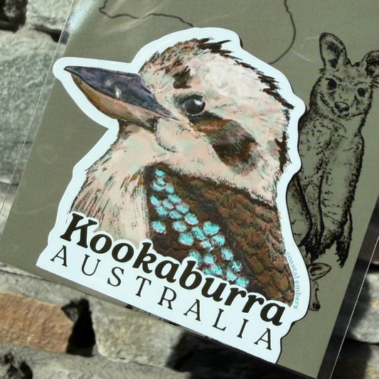 A die-cut sticker featuring a detailed illustration of a kookaburra with the text 'Kookaburra AUSTRALIA' printed below it, attached to a backing card. The backing card also shows a line drawing of a wallaroo and the partial text 'Aussie Mag'.